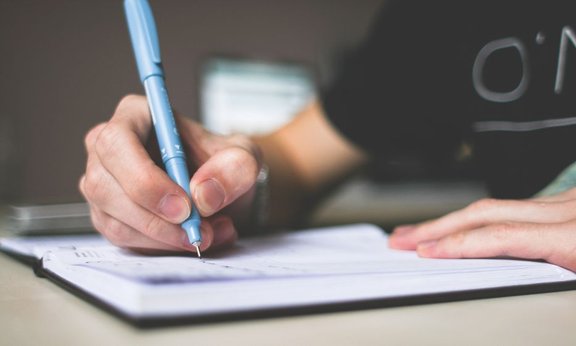 Person schreibt mit einem Stift in ein Notizbuch